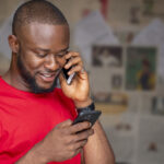A young African male talking on the phone while using another one in a room